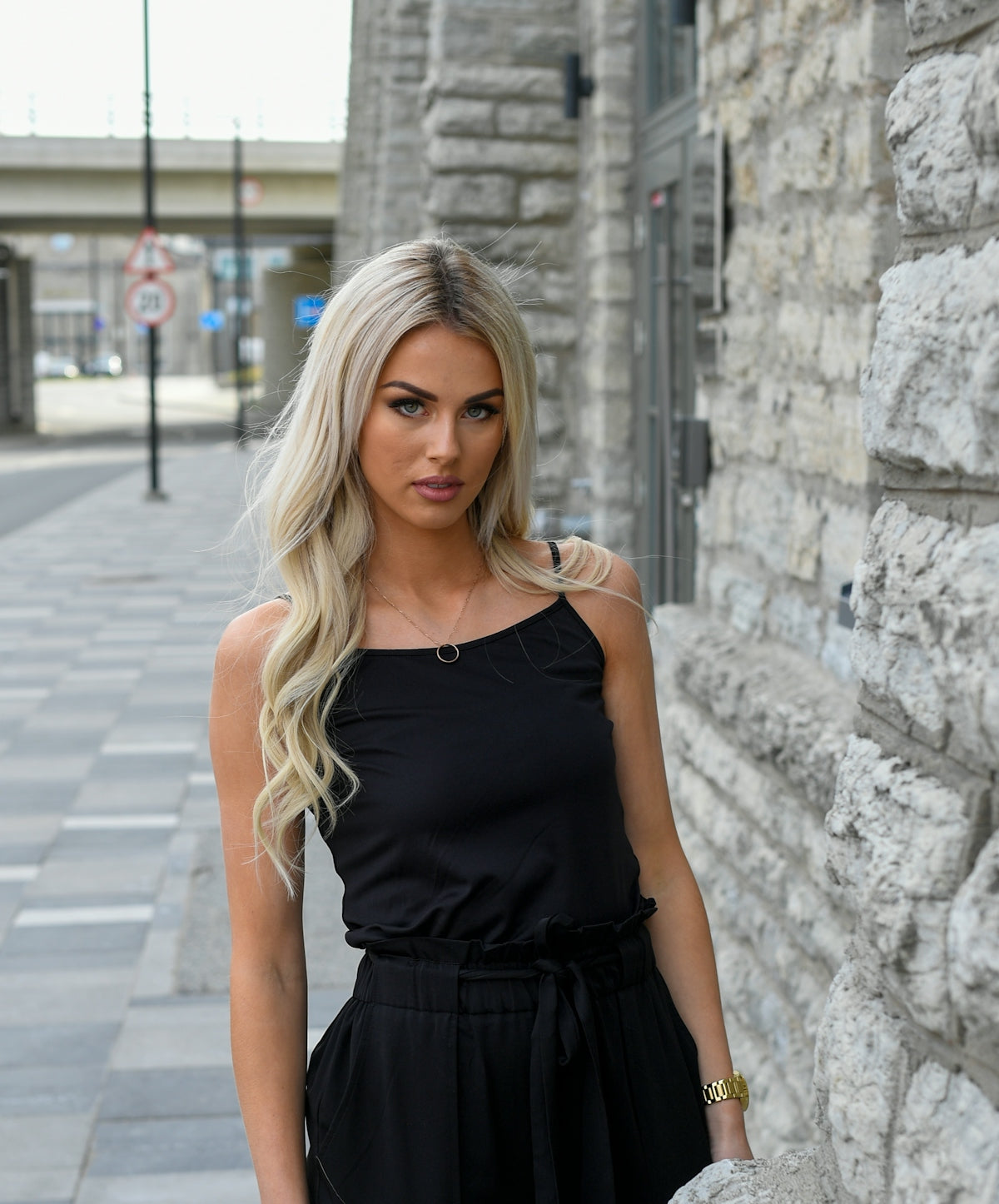A blonde woman in a black outfit stands outdoors.