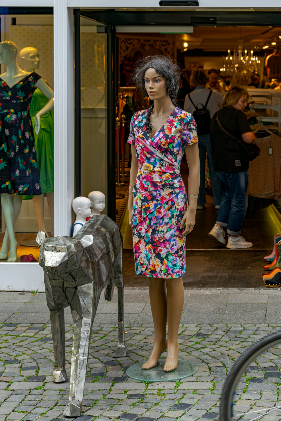 Mannequin in colorful floral dress stands outside a vibrant shop
