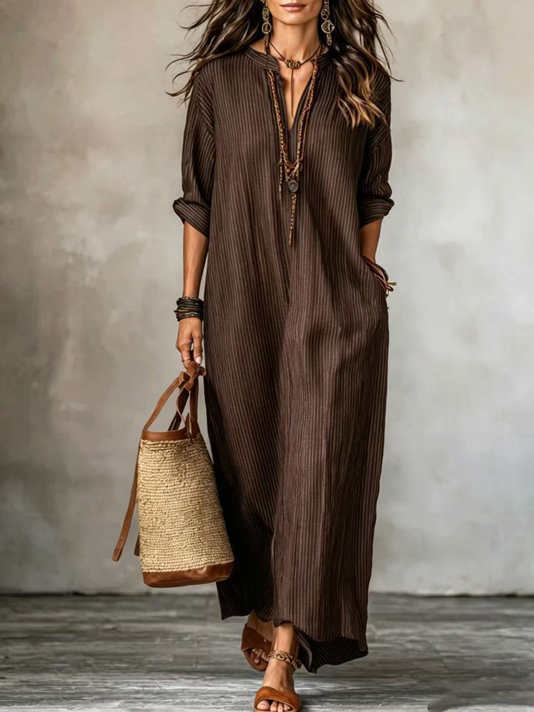 Frau im braunen Längsstreifen Maxikleid mit V-Ausschnitt, dazu Sandalen und Basttasche. IsabellBoutique030