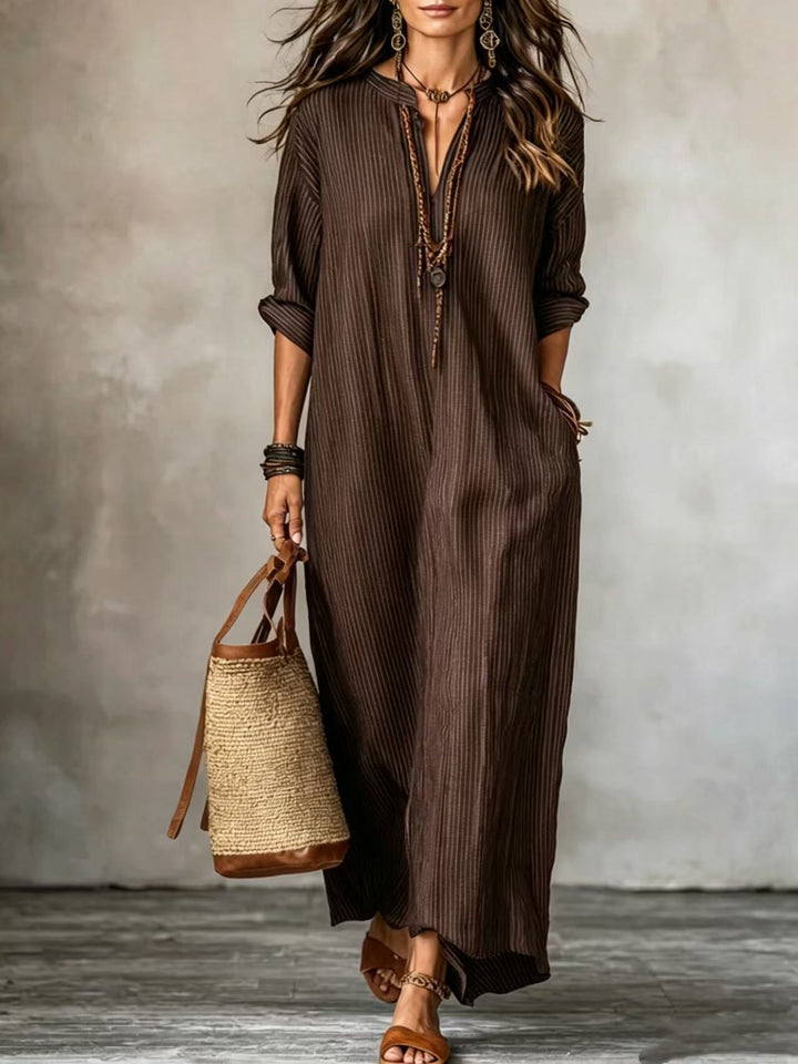 Frau im braunen Längsstreifen Maxikleid mit V-Ausschnitt, dazu Sandalen und Basttasche. IsabellBoutique030