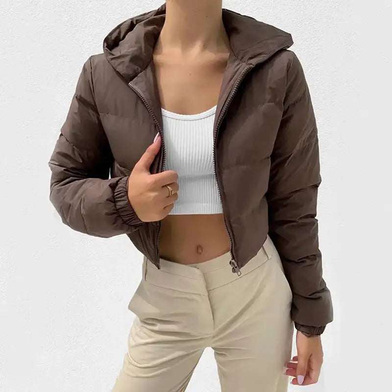 Braune, kurze gesteppte Jacke mit Kapuze und Reißverschluss, kombiniert mit weißem Crop-Top und beiger Hose. IsabellBoutique030.