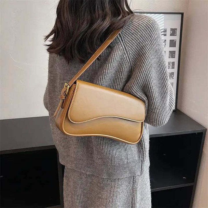 Braune Leder-Schultertasche mit Klappe und schmalem Gurt, getragen über einem grauen Strickpullover. IsabellBoutique030