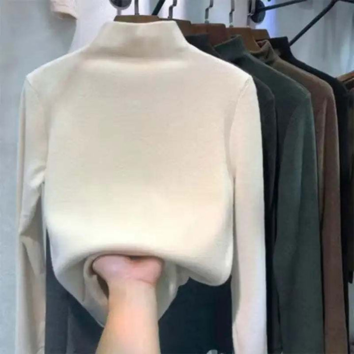 Cremefarbenes Langarm-Rollkragenshirt aus weichem Material, neben dunkleren Farben an Kleiderbügeln gehängt. IsabellBoutique030.