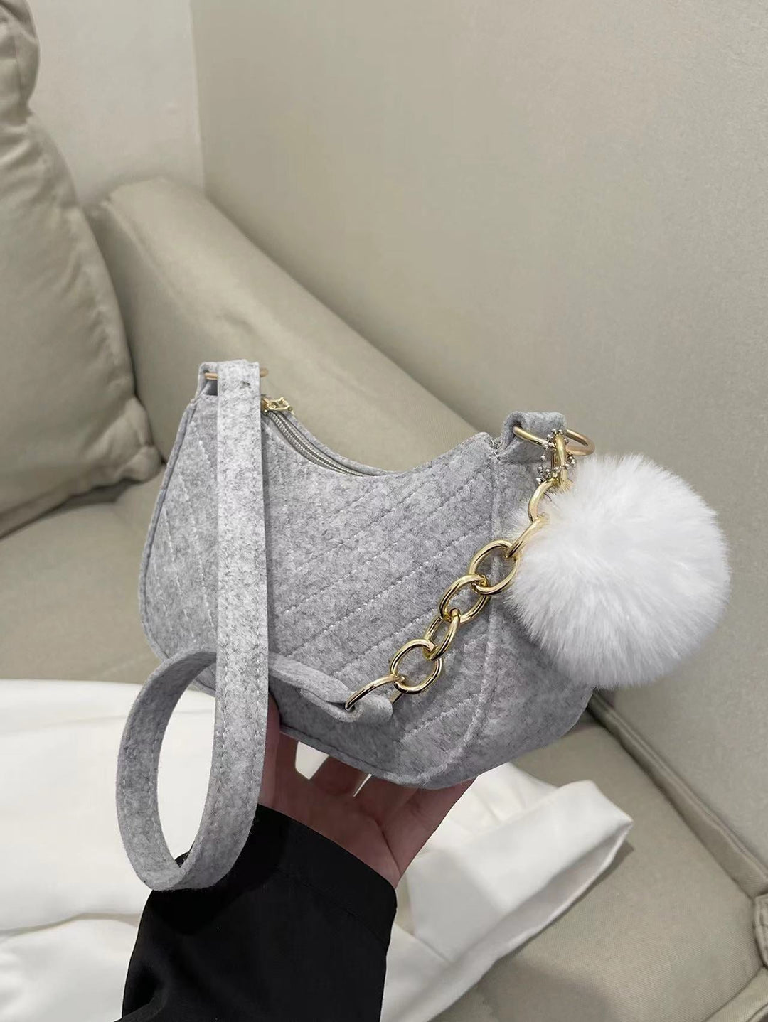 Graue gesteppte Filz-Umhängetasche mit goldenen Kettendetails und weißem Bommel-Anhänger. IsabellBoutique030