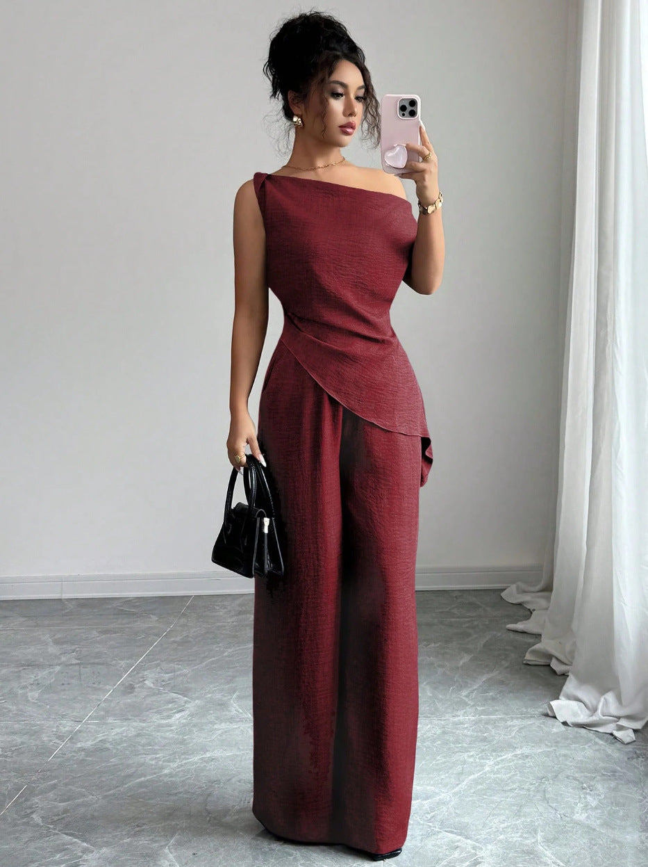 Eine Frau im dunkelroten One-Shoulder-Jumpsuit mit weiten Beinen, modischem Überwurfdetail und schwarzer Handtasche. IsabellBoutique030
