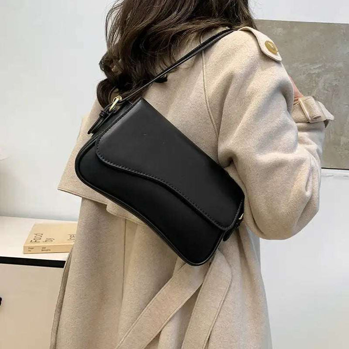 Schwarze Leder-Umhängetasche mit Klappe und goldener Schnalle, getragen über einem beigefarbenen Mantel. IsabellBoutique030
