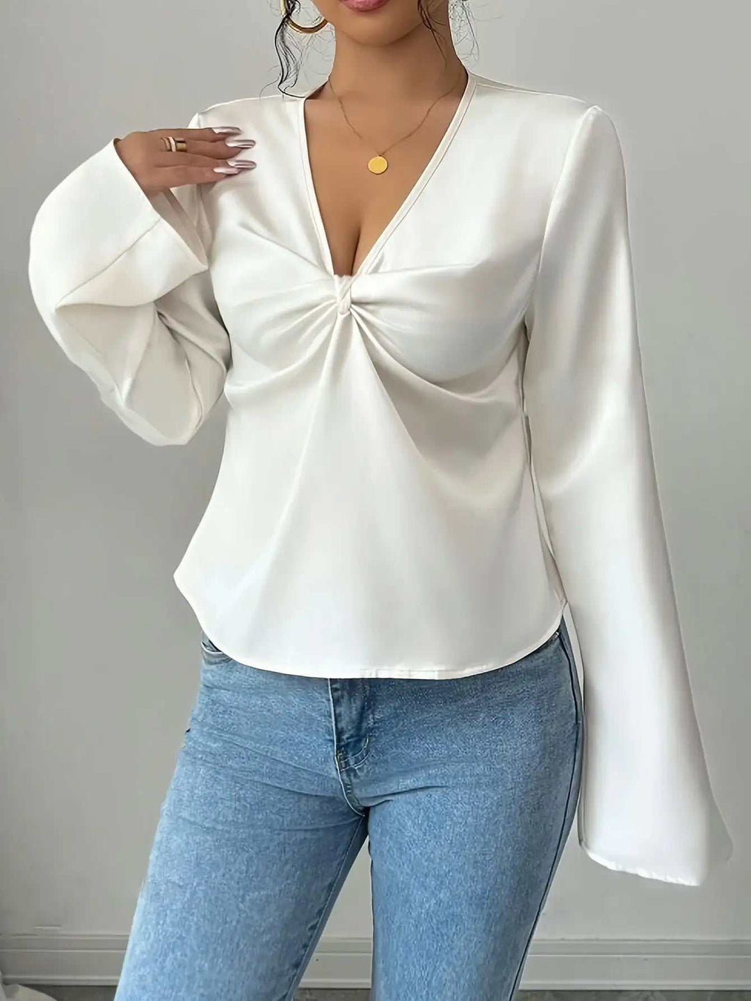 Weiße Bluse mit tiefem V-Ausschnitt und Drapierung vorne, langen Glockenärmeln. Kombiniert mit blauer Jeans. IsabellBoutique030.