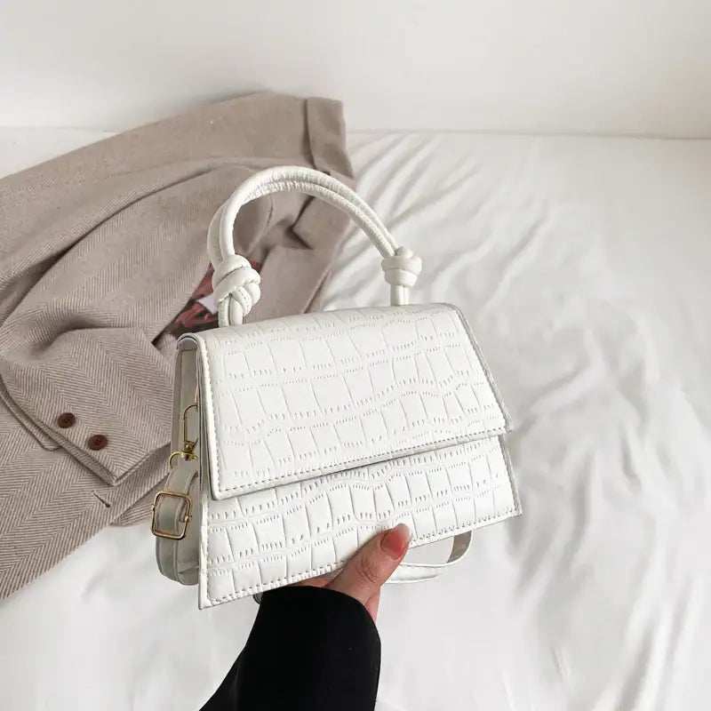 Weiße krokodilgeprägte Handtasche mit verdrehtem Henkel und goldener Schnalle, getragen über einem cremefarbenen Blazer. IsabellBoutique030