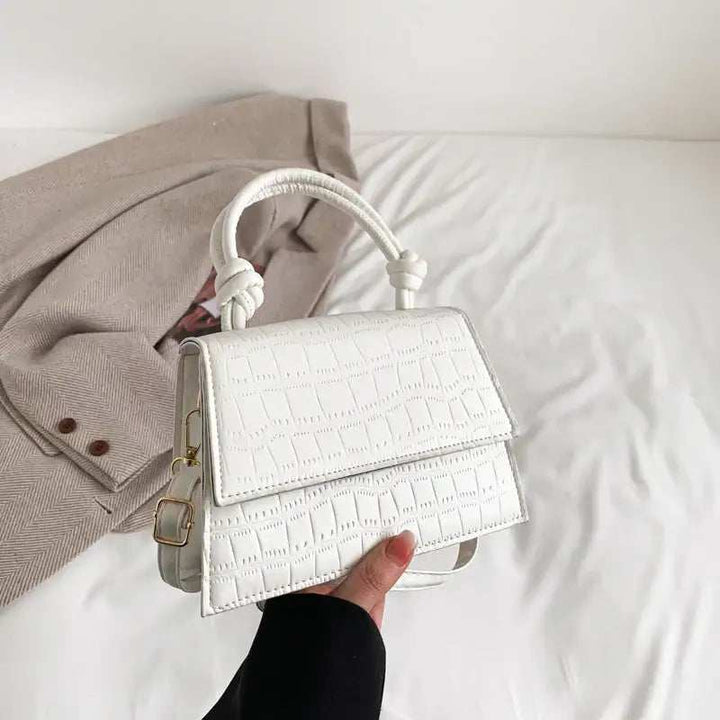 Weiße krokodilgeprägte Handtasche mit verdrehtem Henkel und goldener Schnalle, getragen über einem cremefarbenen Blazer. IsabellBoutique030