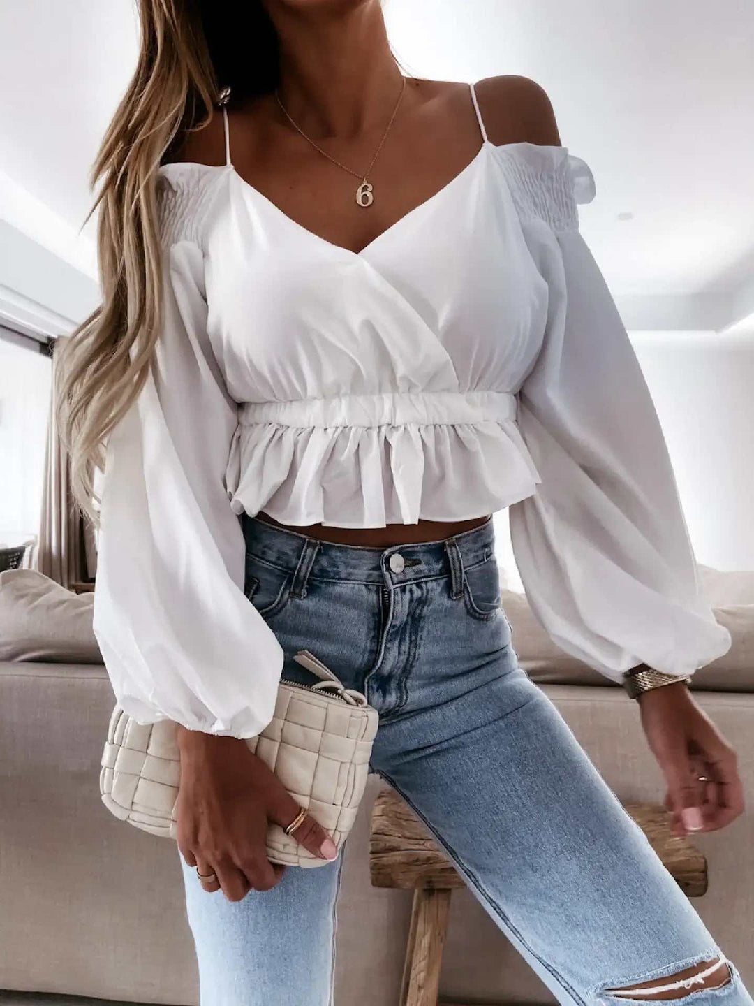 Weißes Off-Shoulder-Oberteil mit Wickeloptik, Puffärmeln und Rüschensaum, kombiniert mit blauer Ripped Jeans. IsabellBoutique030