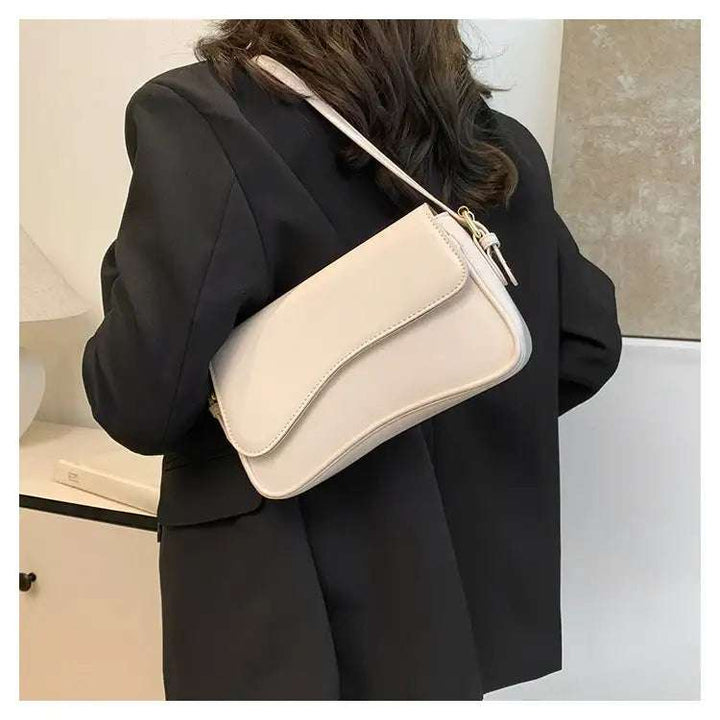 Cremefarbene Schultertasche aus Leder mit geschwungener Klappe, getragen über einem schwarzen Blazer, IsabellBoutique030