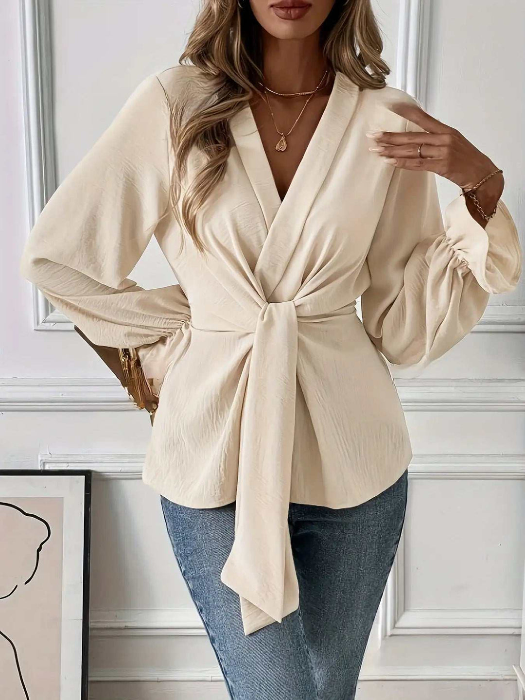 Cremefarbene Wickelbluse mit tiefem V-Ausschnitt, Schleifendetail vorne und Puffärmeln, kombiniert mit Jeans. IsabellBoutique030.